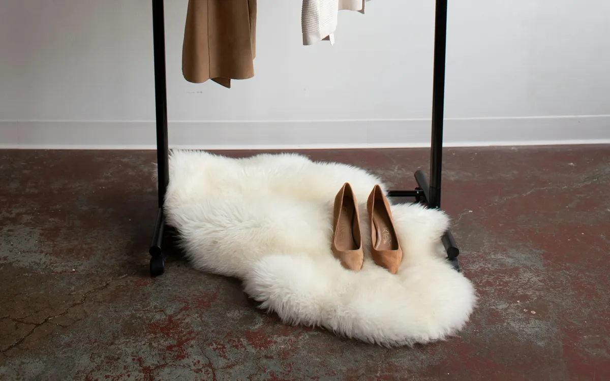 A slim clothes rail with one coat and a pair of shoes on a sheepskin rug