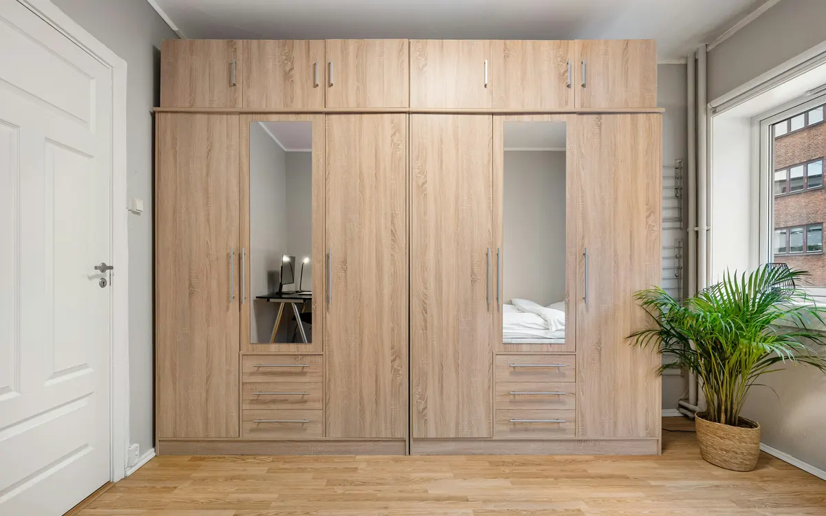 Roupeiro de madeira com portas de abrir e espelhos num quarto claro