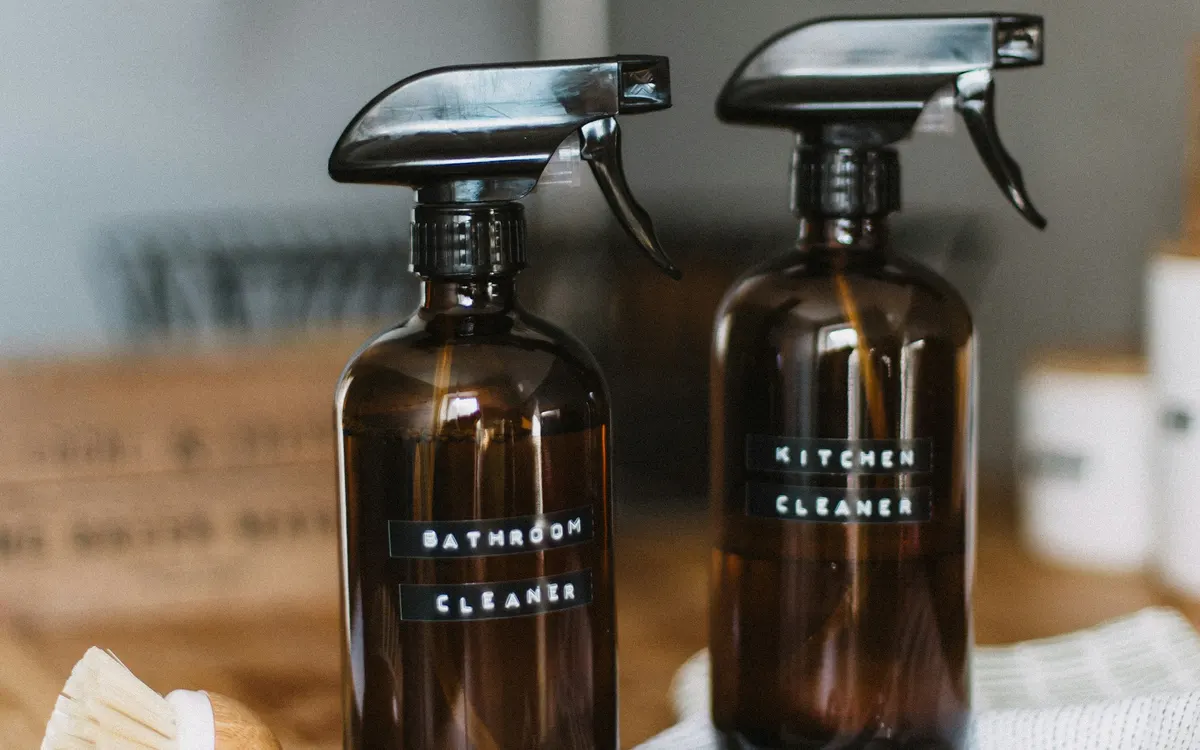 Two refillable amber spray bottles labelled for bathroom and kitchen cleaning