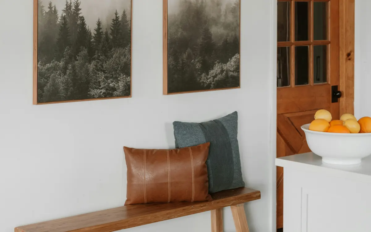 A wooden hallway bench with cushions below two framed prints