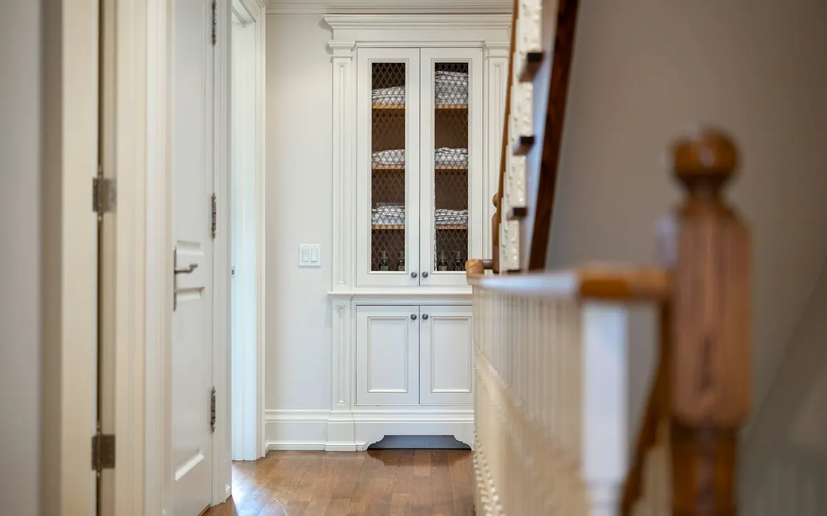 A white built-in cupboard beside a wooden staircase in a hallway